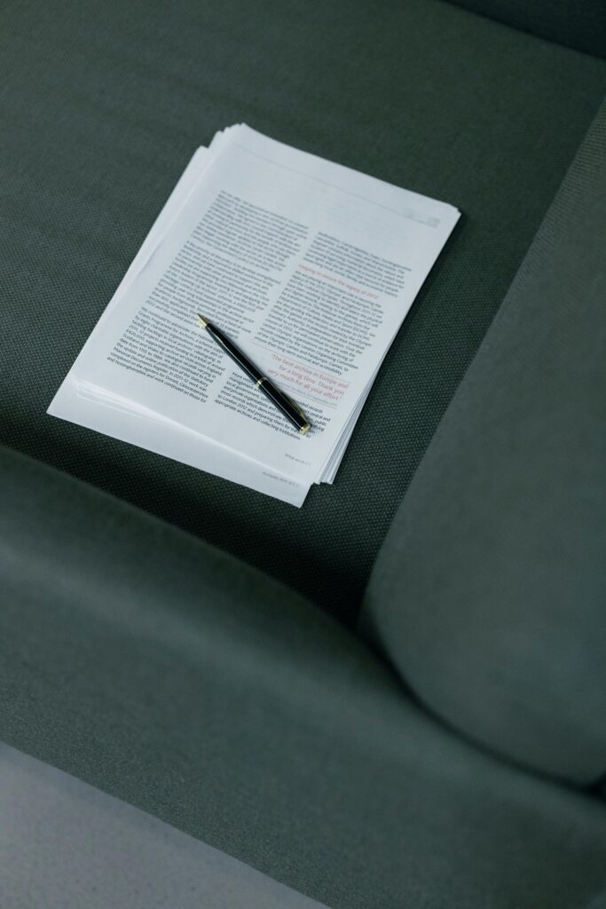 A pen resting on a stack of documents on a dark green sofa.